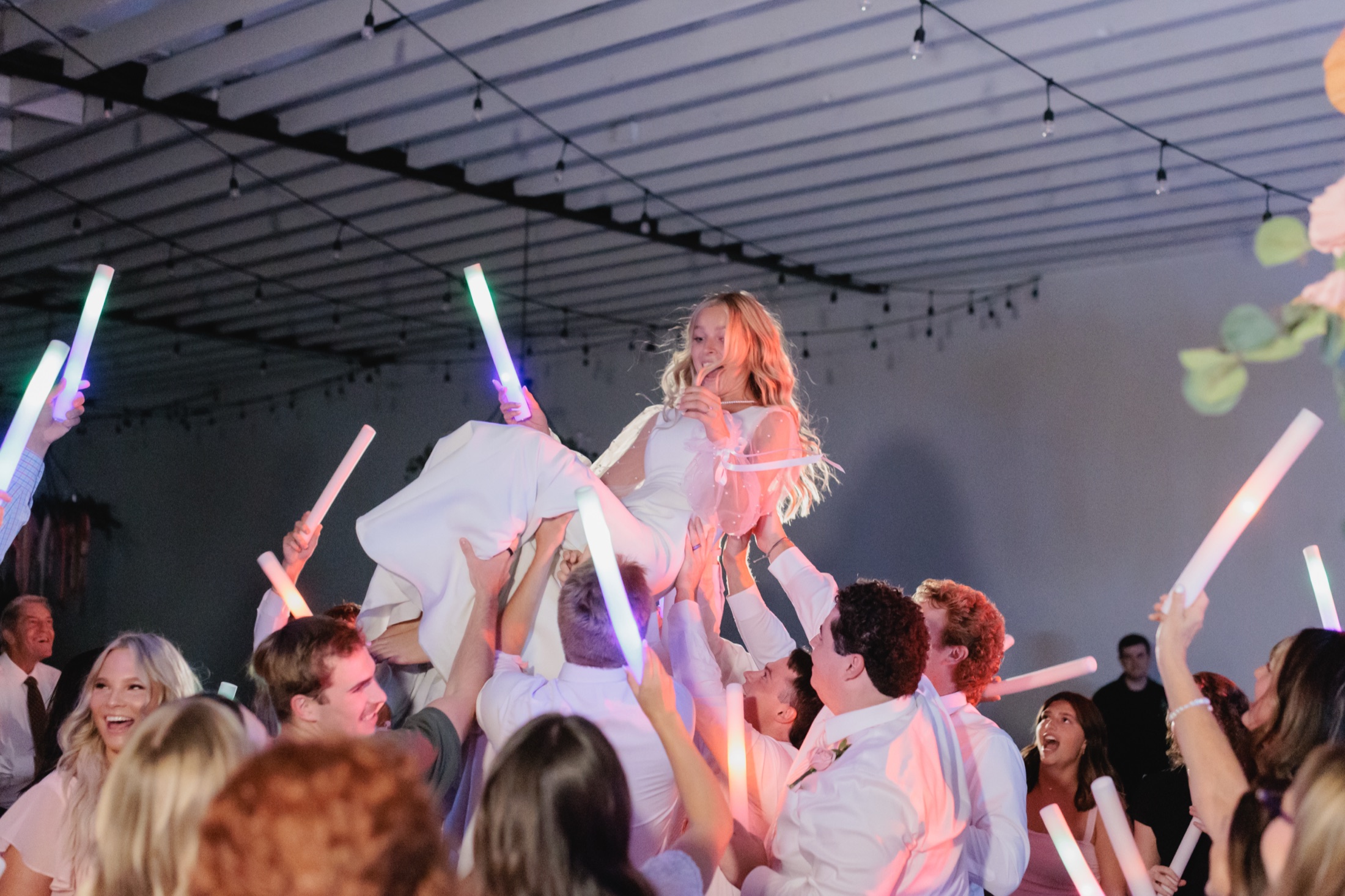 Bride lifted above a packed dance floor while guests raise glow sticks